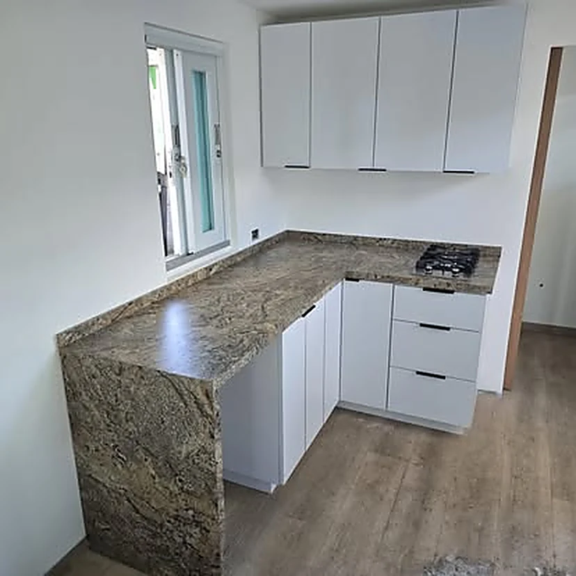 Cocina blanca en L con tope de granito veteado y barra en cascada.