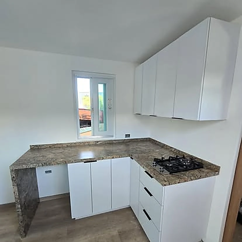 La cocina del plano ya fabricada e instalada: gabinetes blancos, tope de granito, estufa empotrada y gavetería.